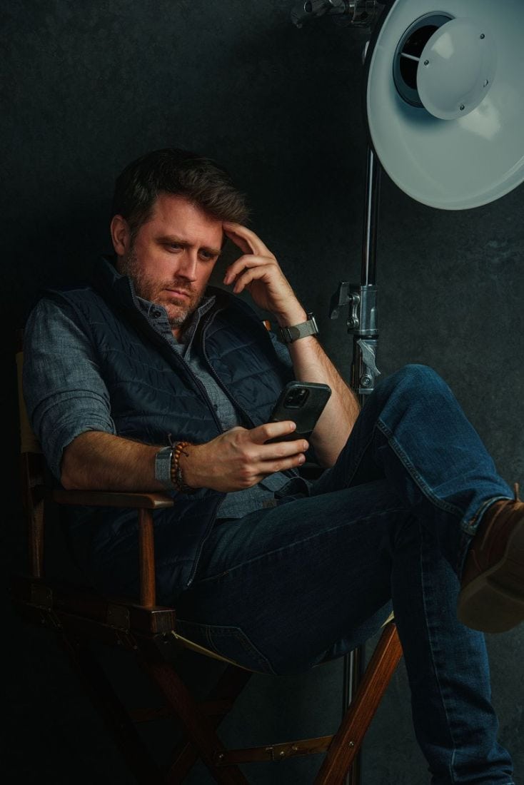 NYC Photographer Nick Coleman seated in signature Manhattan studio, reviewing phone beside pro-grade softbox lighting.
