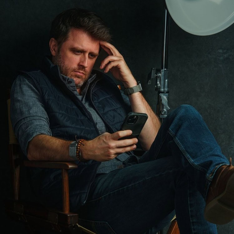 NYC Photographer Nick Coleman seated in signature Manhattan studio, reviewing phone beside pro-grade softbox lighting.
