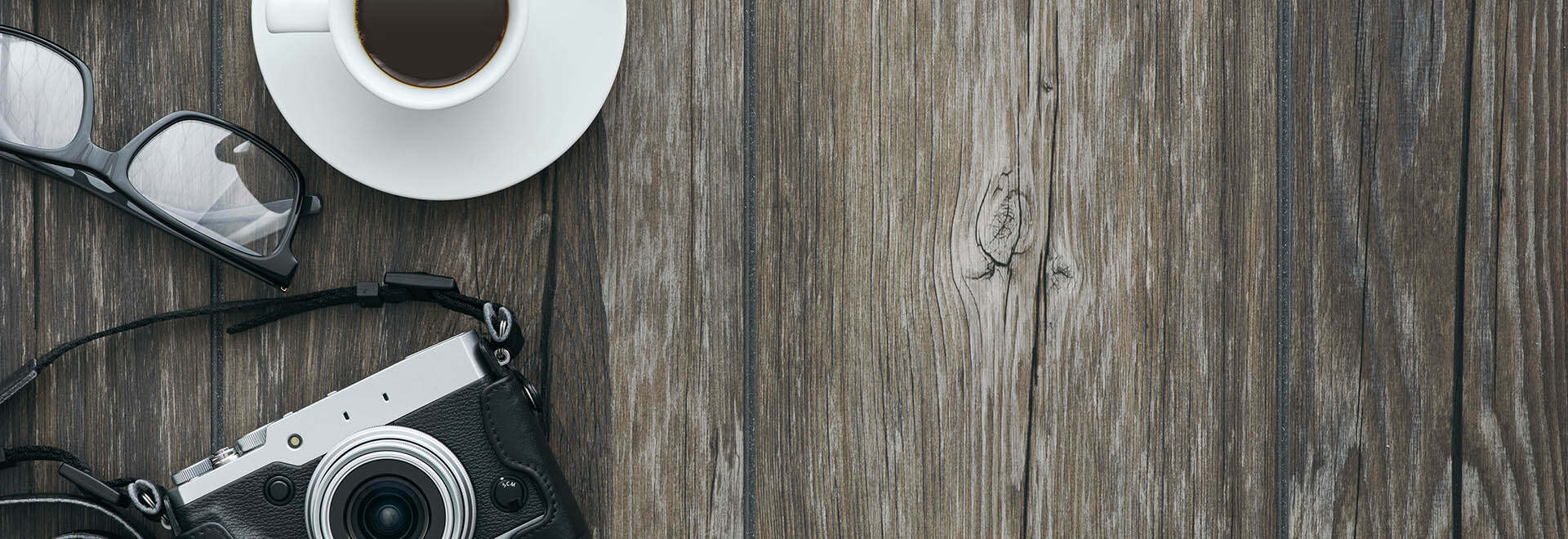 Coffee, eyeglasses, and camera on wooden table with open space to the right for creative work.